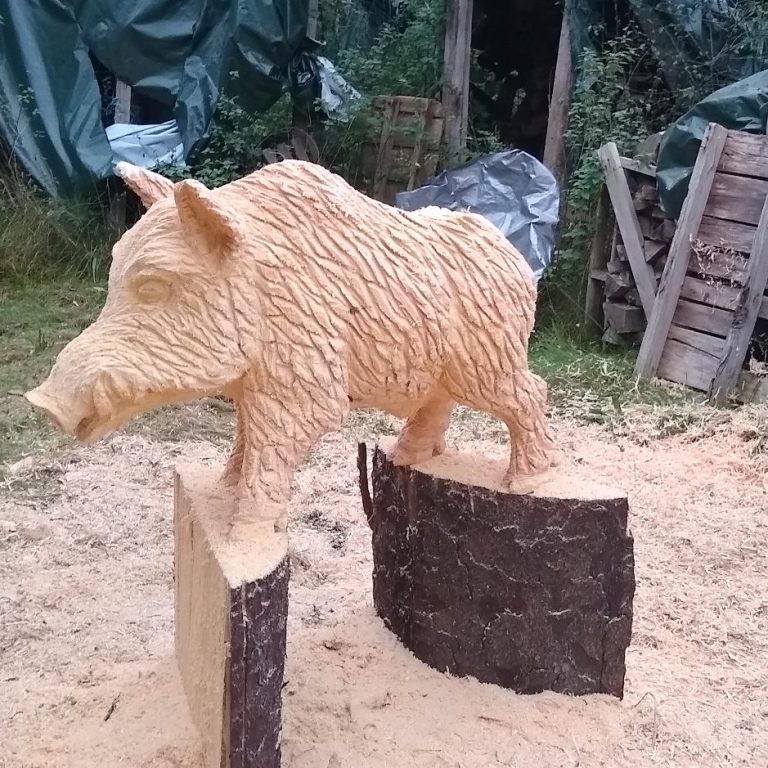 Eule aus Holz, kunstvoll geschnitzt, steht auf einem Stein auf grünem Hintergrund.