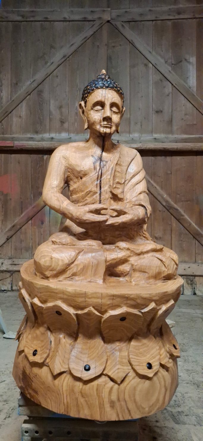 Holzskulptur eines meditierenden Buddhas auf einem kunstvoll geschnitzten Sockel.